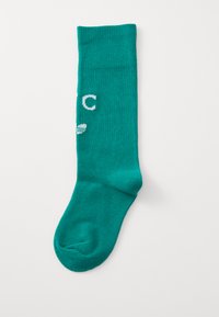 Turkis strikket sokk med en jevn tekstur, med hvit skrift og en buet tådesign. Klassisk midt-legg lengde.