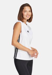 Top deportivo sin mangas de color blanco con un escote redondo, que presenta acentos de rayas negras en los laterales y un pequeño logo en el pecho.