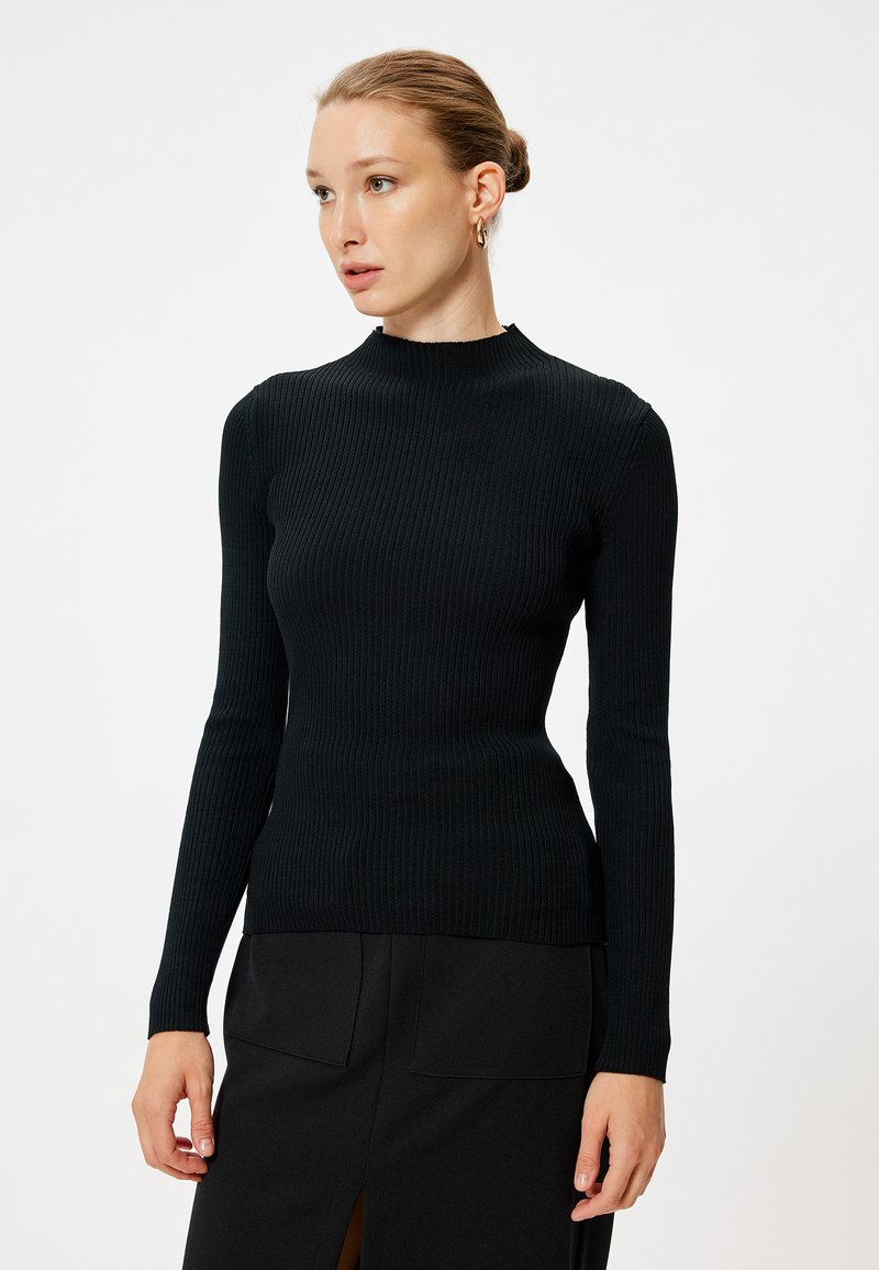 Svart ribbad långärmad topp med mock neck, kroppsnära silhuett och mjuk textur, parat med en svart kjol med en slitsdetalj.