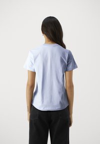 Světle modré bavlněné tričko s klasickým kulatým výstřihem a krátkými rukávy, s volným střihem. Zadní pohled ukazuje hladkou texturu a tvar.