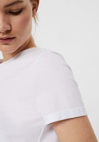 Weißes Baumwoll-T-Shirt mit umgeschlagenen Ärmeln und Rundhalsausschnitt. Glatte Textur mit tailliertem Schnitt und sichtbaren Nahtdetails.