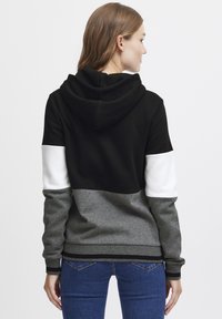 Hettegenser med fargeblokk-design i svarte, hvite og grå seksjoner. Mykt stoff med ribbestrikkede mansjetter og nederkant.