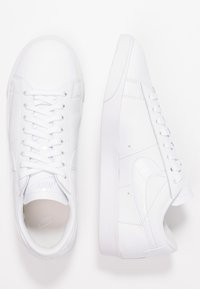 White leather sneakers with a smooth texture, featuring a low-top design, round toe, flat rubber sole, and lace-up closure.