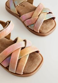 Sandalice s metalnim, ukriženim tekstilnim gornjištem u pastelnim nijansama; mekana bež suđena unutrašnjost; ojačana traka s okruglim metalnim detaljem.