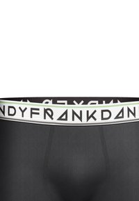 Schwarze gerippte Boxershorts mit einem weißen Bund, der schwarzen Text und eine grüne Akzentlinie aufweist. Glatte Textur, enganliegendes Design.
