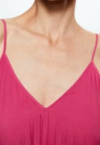 Haut rose sans manches avec un col en V. Le tissu semble doux avec une texture subtile. Les bretelles réglables améliorent l'ajustement.