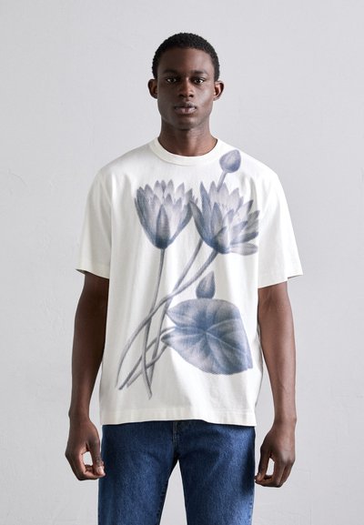 Kortærmet hvid bomulds T-shirt med et blåt blomsterprint af liljer og blade, med en afslappet pasform og rund halsudskæring.