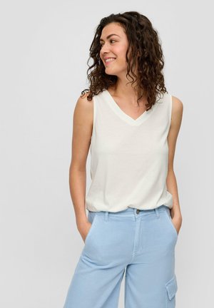 Lockere cremefarbene, ärmellose Bluse mit V-Ausschnitt und weichem Stoff, kombiniert mit hellblauen, weit geschnittenen Hosen mit Seitentaschen.