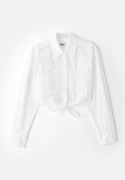 Witte cropped shirt met een puntkraag, een sluiting met knopen aan de voorkant en textuurkantdetails in het midden; gestrikt aan de taille.
