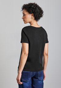 Zwart t-shirt met korte mouwen en ronde halslijn, gemaakt van een gladde katoenstof en met een losse pasvorm, gecombineerd met donkerblauwe jeans.