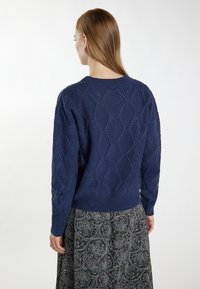 Marineblauwe gebreide trui met een gestructureerd ruitpatroon, geribbelde manchetten en zoom. Draagt met een patroonskirt, achteraanzicht weergegeven.