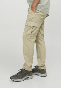 Beige Cargo-Hosen mit Seitentaschen, aus einem Baumwollmischgewebe. Verfügt über einen geraden Beinschnitt und einen lässigen Fit. Kombiniert mit dunklen Sportschuhen.