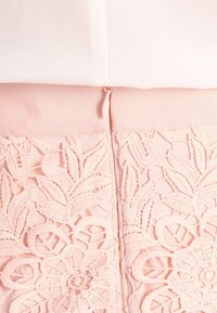 Pink floral lace detail on a garment with a soft texture and a waistband featuring ribbed fabric. Hidden zipper at the back.