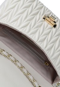 La borsa in pelle trapuntata bianca presenta all'interno una tasca con zip, hardware dorato e una tracolla a catena con accenti piatti. Superficie texturizzata per una migliore presa.