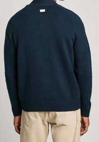 Laivastonsininen neulepaita, jossa on resorit helmassa ja hihoissa, ja pieni vaalea etiketti takakauluksessa. Sileä pinta ja normaali istuvuus.