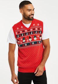 Rode gebreide vest met V-hals, versierd met witte stippen en een patroonband met sneeuwvlokken, gnomes en feestdagen thema's.