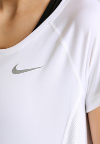 Camiseta deportiva blanca con paneles de malla transpirables, mangas cortas y logo reflectante plateado de Nike en el pecho. Textura de tela suave.