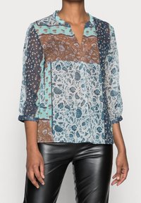 Blusa a più motivi con design floreali, geometrici e paisley in teal, blu navy, marrone e bianco. Maniche a metà con colletto.