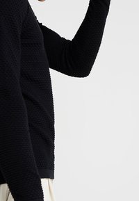 Camicia nera a maniche lunghe con textura e motivo a coste, con silhouette aderente, colletto a giro e orlo a contrasto.