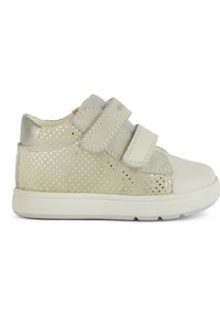 Zapatilla blanca con acentos metálicos, que presenta un diseño de perforaciones punteadas, dos correas de Velcro y una puntera suave y redondeada.