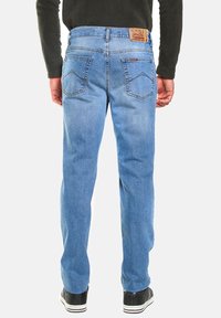 Jeans de mezclilla azul claro con corte recto, bolsillos traseros y una etiqueta de cuero en la cinturilla. Combinados con zapatillas negras.