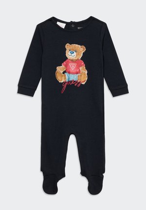 Pijama negro para bebé con pies y manga larga con un oso de peluche vestido con una camiseta roja Guess y pantalones cortos azules estampados en el pecho.