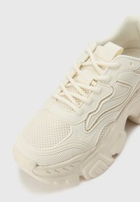 Baskets blanches épaisses avec une tige en maille texturée, des accents en caoutchouc lisses et une semelle épaisse. Dotées d'un laçage proéminent et d'une zone de bout renforcée.