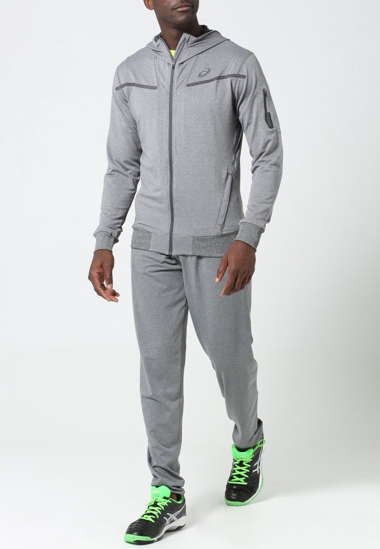 Grijze sportieve trainingspak met een capuchon, voorzien van een rits aan de voorkant, zijzakken en zwarte accenten. Draagt een paar zwart-groene sneakers.