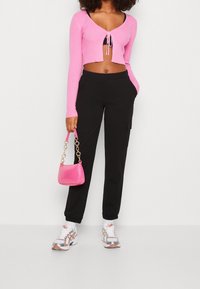 Růžový žebrovaný crop top s vázáním v přední části, černé cargo kalhoty s kapsami a malá růžová kabelka s embosovaným krokodýlím vzorem. Bílé a stříbrné tenisky.