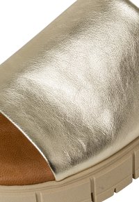 Metalen gouden slip-on sandaal met een gladde bovenkant, een bruine binnenvoering en een dikke beige zool met geribbelde textuur.