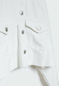 Bílé džíny s kovovými knoflíky, náprsními kapsami a roztrhanými okraji, s texturovanou látkou a zkráceným střihem.