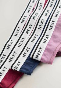 Mehrfarbige Baumwollslips gestapelt, mit weißen elastischen Bändern, auf denen "NEXT" in Schwarz gedruckt ist. Die Farben umfassen Burgunderrot, Marineblau und Pink.