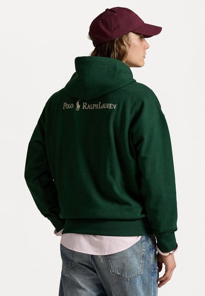 Grøn hoodie med en stor hætte, ribbet kant og manchetter. Har "Polo Ralph Lauren" logo i beige på ryggen. Bæres over en lys pink skjorte.