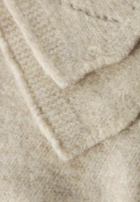 Tessuto di lana beige chiaro, con una consistenza morbida e pelosa. Presenta un design a strati, che mostra motivi variati e una finitura liscia e bordata.