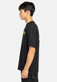 Black cotton t-shirt with short sleeves, featuring a yellow logo on the chest and a side. Standard crew neck design.