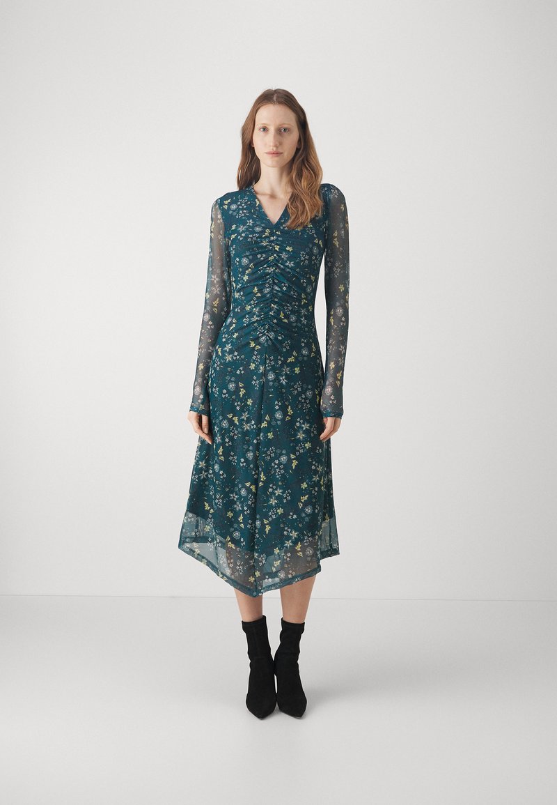 Abito teal con stampa floreale, dotato di un corpetto fitted e arricciato e maniche lunghe trasparenti. Accentuato da una gonna fluida e trasparente, abbinato a stivali neri alla caviglia.
