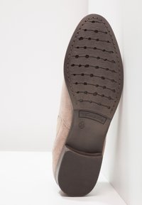 Vaaleanpunaiset mokkasiinit, joissa on tekstuurinen ruskea kumipohja, joka sisältää joustavan, kuviollisen kulutuspinnan ja kohokuvioidut bränditiedot. Koko 38.