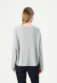 Svetlo sivi oversized pulover s okroglim izrezom, spuščeni rameni in dolgimi rokavi. Mehak material in rebrast rob na hrbtni strani.