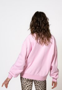 Rosa Sweatshirt mit lässiger Passform, überschnittenen Schultern, gerippten Bündchen und Saum. Kombiniert mit Leggings im Tierdruck, die ein strukturiertes Muster präsentieren.