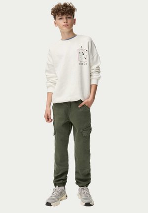 Sudadera blanca con gráfico de Pikachu, pantalones cargo verdes con bolsillos laterales y zapatillas grises con acentos blancos. Conjunto casual para jóvenes.