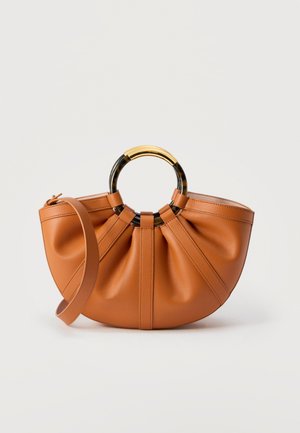 Barna bőrtáska ráncolt részletekkel, kör alakú fekete és arany teknősbéka mintás fogantyúval, valamint levehető vállpánttal, fehér háttéren.