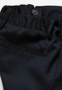 Mørkeblå bukser med tekstureret stof, der har en elastisk talje, knaplukning og en baglomme med en synlig sømkant.