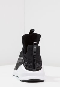 Svart atletisk sko med en texturerad ovandel av tyg, slankt design, böjd vit sula och reflexdetaljer vid hälen och baksidan.