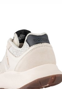 Baskets beige clair avec maille texturée blanc cassé et accents en daim, languette de talon noire avec le logo "WODEN" et semelle en caoutchouc pour une meilleure traction.
