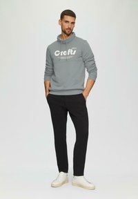 Felpa grigia con collo alto e stampa bianca "crafts", abbinata a pantaloni neri e sneaker bianche. Tessuto liscio e design aderente.