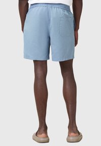 Pantalones cortos azul claros con cintura elástica, un bolsillo trasero y una textura suave, combinados con zapatos de lona beige.