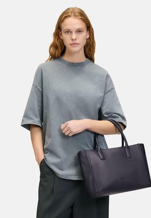 Graues Übergrößenhemd mit kurzen Ärmeln, kombiniert mit einer dunkelblauen Ledertasche mit doppelten Griffen und strukturierter Oberfläche.