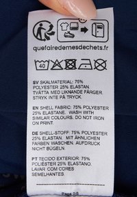 Etykieta pielęgnacyjna na tkaninie; biała z czarnym tekstem, symbolami prania i wielojęzycznymi instrukcjami. Materiał: 75% poliester, 25% elastan.