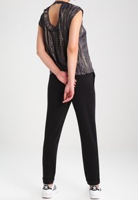 Black, loose-fitting pants with a smooth texture and cuffed hems, paired with a metallic short-sleeve top featuring a keyhole back design.