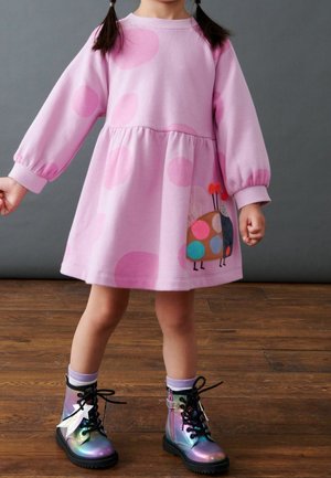 Pink pullover dress with large light pink dots, gathered waist, and a colorful bird design. Paired with multicolored shiny ankle boots.